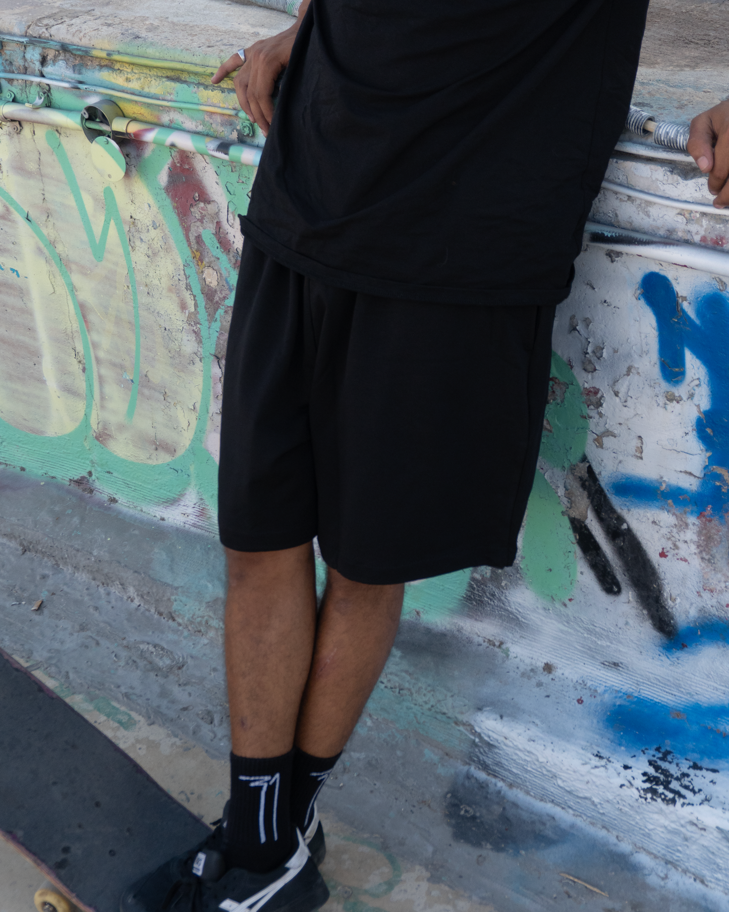 Back view of OKRUG 31 black relaxed shorts worn in a graffiti skatepark