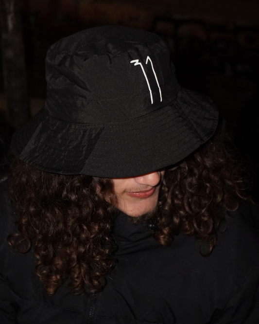 Person wearing a black bucket hat with a logo in a dark setting