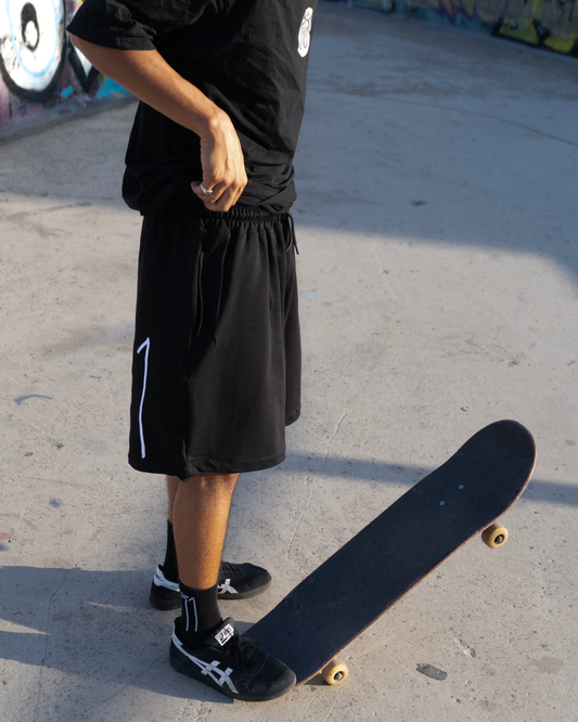 Model wearing OKRUG 31 black shorts with white side logo beside a skateboard