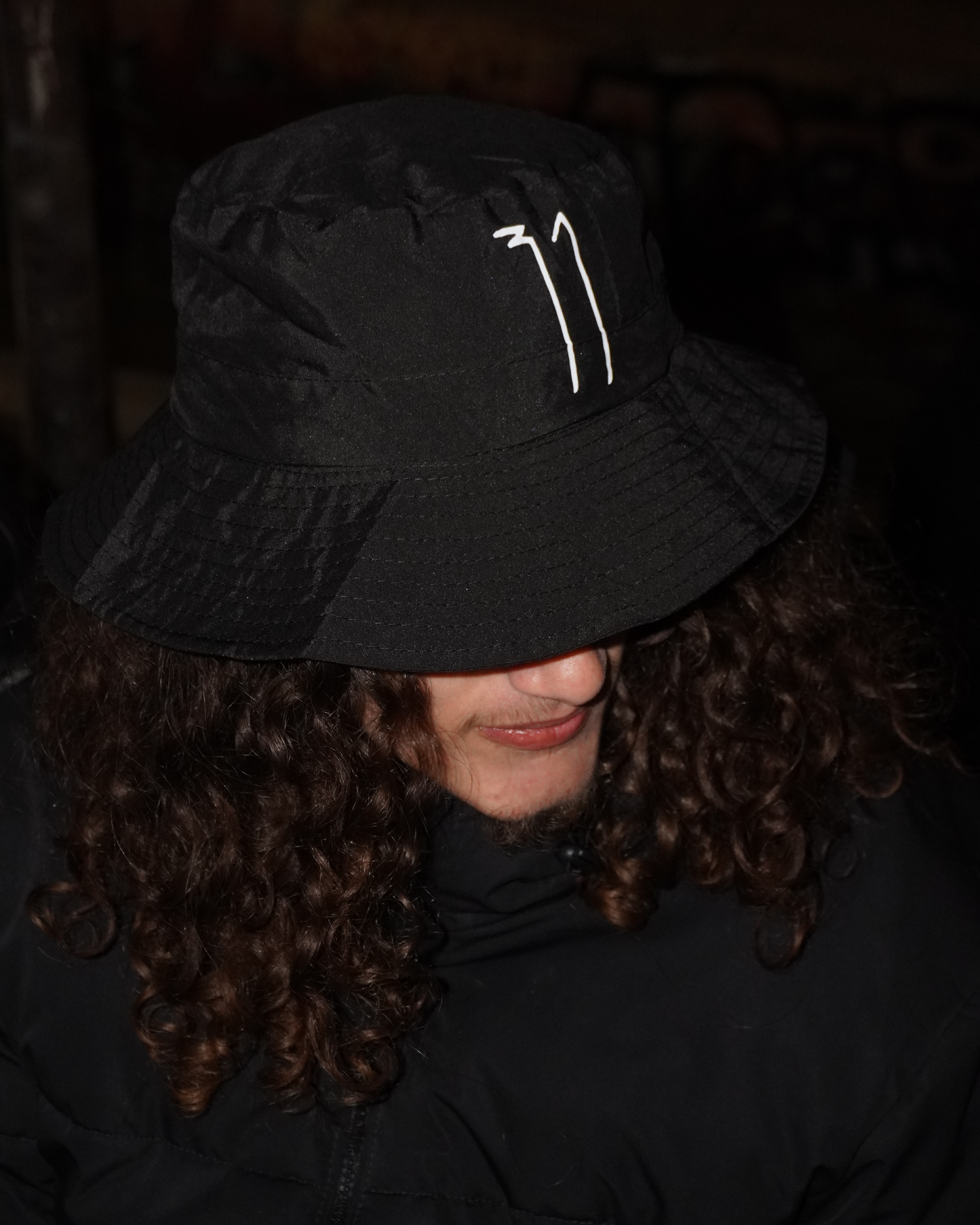 Person wearing a black bucket hat with a logo in a dark setting